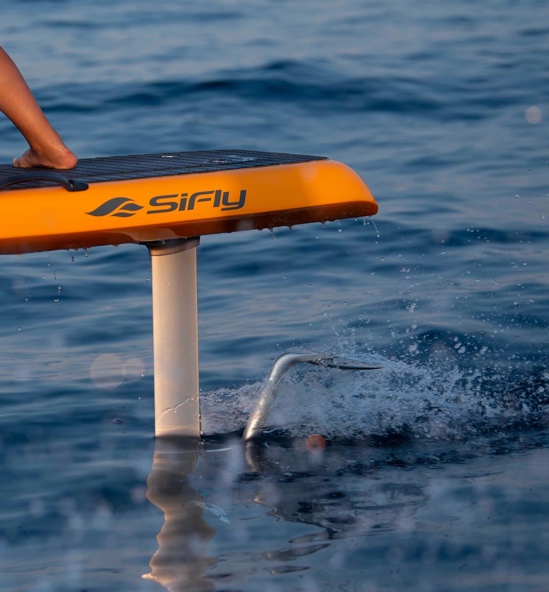 Close-up of orange SiFly eFoil board hull lifted above ocean surface, white hydrofoil mast submerged with water dripping from